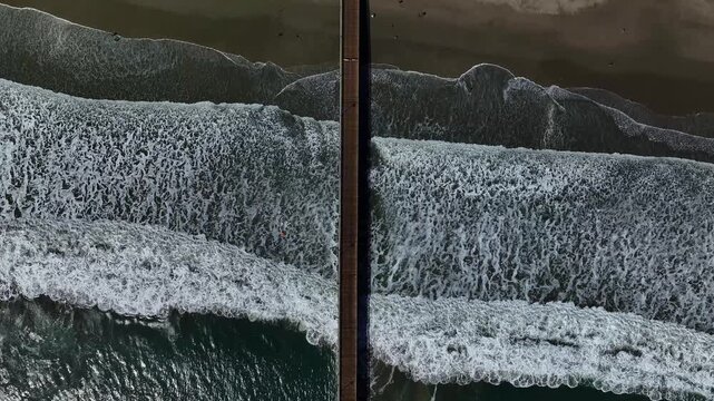 Aerial view of the Pismo Beach Pier contrasts with the foamy white waves crashing onto the sandy shore, showcasing nature's power, Pismo Beach, California, United States.