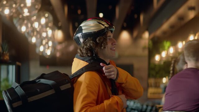 Food delivery courier in bicycle helmet entering the restaurant to pick up order for delivery. Shot with 2x anamorphic lens