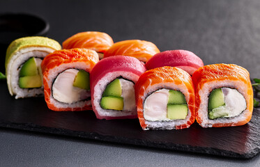 Colorful assorted sushi rolls with salmon, tuna, avocado, and cucumber, on a black stone plate, minimal background, perfect for advertising
