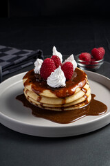 pancakes with chocolate syrup, cream, and raspberries on a round gray plate seen from a 45-degree angle