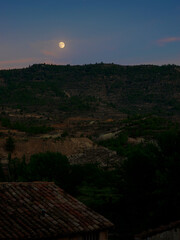 Rural mountain scene at dusk with moon rising above the horizon