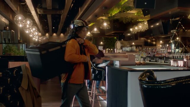 Food delivery courier in bicycle helmet entering the restaurant to pick up order for delivery. Shot with 2x anamorphic lens