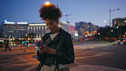 Night girl messaging mobile phone standing by lively urban road closeup.