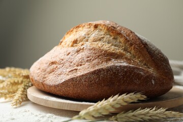 Loaf of fresh bread, flour and spikes on table, closeup