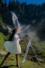 Artist woman drawing outdoor. Painting art. Woman artist draw pictures in alps mountain. Woman painting with brushes oil or acrylic paint. Female artist paints a picture on canvas.