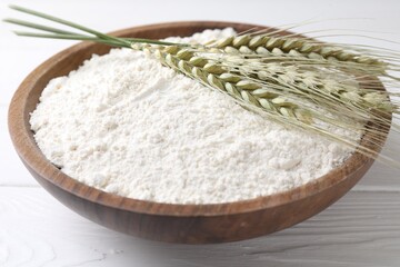 Flour and green wheat spikes in bowl on white wooden table, closeup