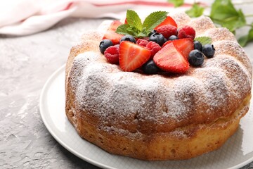 Tasty Bundt cake with powdered sugar and berries on grey textured table, closeup