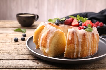 Pieces of delicious bundt cake with berries, glaze and mint on wooden table, closeup
