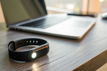 Fitness tracker, Smart fitness tracker beside a laptop on a wooden desk in a modern workspace.