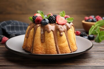Tasty Bundt cake with berries, chocolate and mint on wooden table, closeup