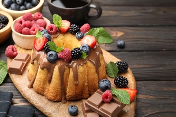 Tasty Bundt cake with berries, chocolate, mint and coffee on wooden table, closeup. Space for text