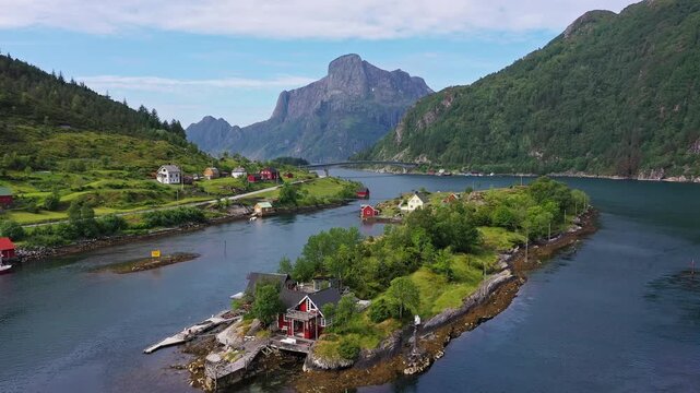 Aerial view of quaint houses with red roofs nestled on small islands connected by a bridge, amidst the fjords and lush greenery, Rugsund, Vestland, Norway.