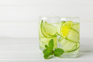 Cucumber water with lemon, lime and mint on a wooden table. Water infused with sliced ​​cucumber in a drinking glass. Tonic refreshing drink. Cucumber lemonade.Summer natural cooling drink.Copy space