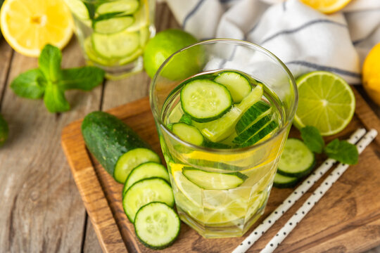 Cucumber water with lemon, lime and mint on a wooden table. Water infused with sliced ​​cucumber in a drinking glass. Tonic refreshing drink. Cucumber lemonade.Summer natural cooling drink.Copy space