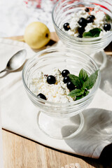 Glass dessert bowls with cottage cheese, black berries, fresh mint and honey on a wooden board. Light summer snack or healthy breakfast idea.