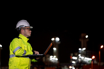 Industrial engineer night inspection at refinery or petrochemical plant walkie-talkie hand and digital tablet intersection of technology, worker work at night at power plant
