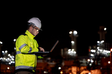 Industrial engineer night inspection at refinery or petrochemical plant walkie-talkie hand and digital tablet intersection of technology, worker work at night at power plant