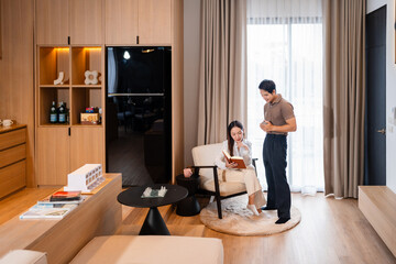 Young couple man and woman asian husband and wife in a relationship reading book hold books sits on armchair at home in the apartment reading leisure bonding family concept . copy space.