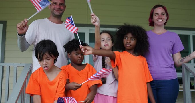 Slow motion Diverse group of children and two adults teacher celebrating outdoors with waving American flags on U.S. Independence Day.enjoying a festive patriotic event