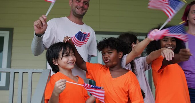Slow motion Diverse group of children and two adults teacher celebrating outdoors with waving American flags on U.S. Independence Day.enjoying a festive patriotic event