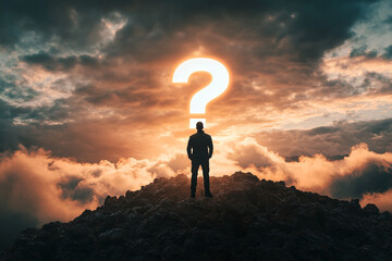 Man on mountaintop contemplating a question mark in the sunset sky