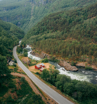 Aerial view of a winding road adjacent to a rushing river, nestled between verdant, tree-covered hillsides, Vindhellavegen, Borgund, Vestland, Norway.