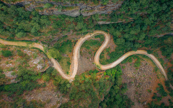 Aerial view of a winding road snaking through a lush, verdant landscape with rocky terrain and dense forestry, Vindhellavegen, Borgund, Vestland, Norway.