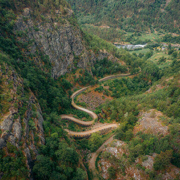 Aerial view of a winding road snaking through a lush, green valley nestled between rugged, rocky cliffs, Vindhellavegen, Borgund, Vestland, Norway.