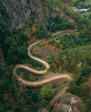 Aerial view of the winding Vindhellavegen road snaking through the steep, verdant valley, a ribbon of stone against the rugged landscape., Borgund, Vestland, Norway.