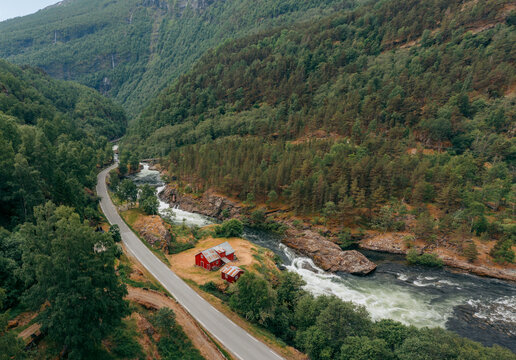 Aerial view of a winding road alongside a vibrant river, cascading through a valley, with red houses nestled near the riverbank, Borgund, Vestland, Norway.