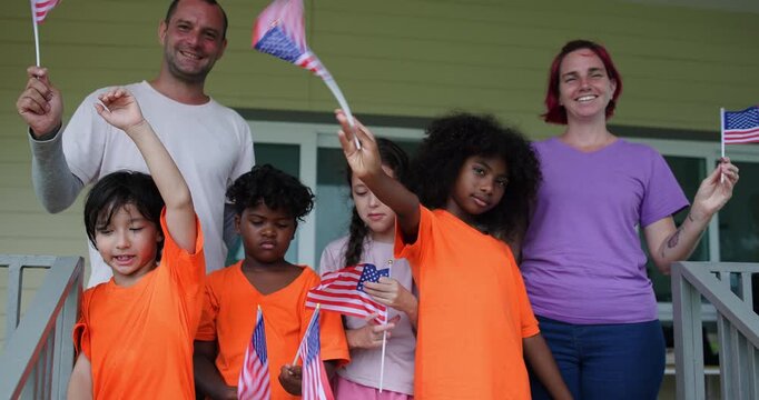 Slow motion Diverse group of children and two adults teacher celebrating outdoors with waving American flags on U.S. Independence Day.enjoying a festive patriotic event