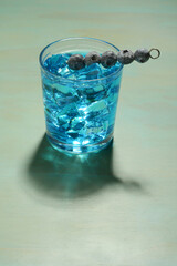 blue cocktail with blueberries in tumbler glass