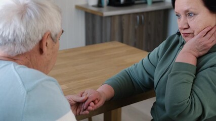 Old couple have breakfast sitting at the kitchen table, drink coffee. Embracing elderly man and woman. Senior couple together marriage in retirement talking with each other. Enjoying the pleasantries - Powered by Adobe