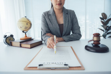 Legal Agreement Presentation: A professional individual in a blazer, poised at a desk, presents a legal document, pen in hand, alongside a gavel and other symbolic items.