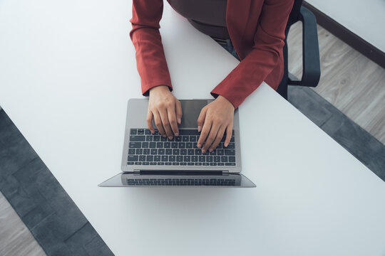 Laptop interaction at work: A top-down perspective captures a professional engrossed in her tasks, typing diligently on a modern laptop set upon a sleek, uncluttered desk.