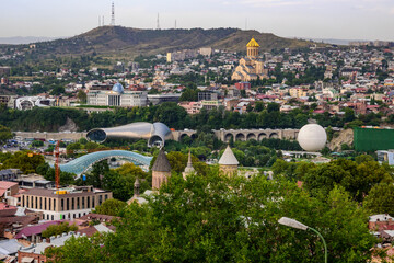 Fototapeta premium Urban panorama showing the juxtaposition of old churches with contemporary structures like the Peace Bridge and the Rike Park Concert Hall, showcasing Tbilisi's evolving identity.