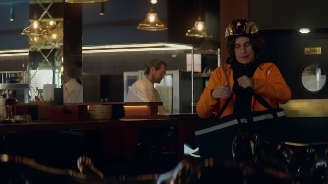 TRACKING CU Portrait of food delivery courier in bicycle helmet leaving a restaurant after picking up order for delivery. Shot with 2x anamorphic lens