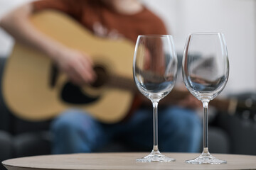 Empty wineglasses on table and man playing guitar indoors, selective focus
