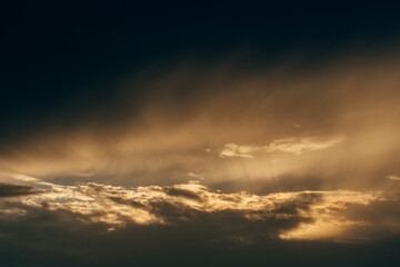 A glowing golden sunset illuminates layered clouds with soft shadows, capturing the serenity and beauty of an evening sky.