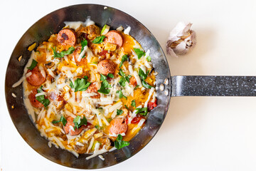 Omelet with vegetables, sausages and parsley cheese in a pan on a white table. View from above.