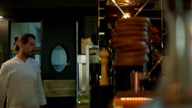 TRACKING Caucasian male chef walking in commercial restaurant kitchen through the swinging doors. Shot with 2x anamorphic lens