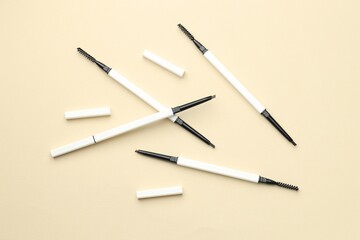 Automatic eyebrow pencils on beige background, flat lay