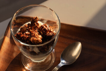 Close-up of a yogurt and homemade vegan and gluten-free granola for breakfast, disposed in a glass on a wooden tray.