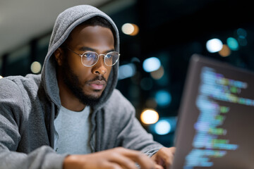 Young man in hoodie and smart glasses coding on laptop in tech hub, RGB lighting, portrait with laptop screen reflection, 