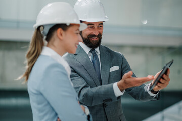 Smiling engineers using tablet discussing project wearing suits and hardhats