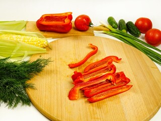 Sliced  raw red bell peppers,  half of pepper, various vegetables are on wooden cutting board, a making of a salad