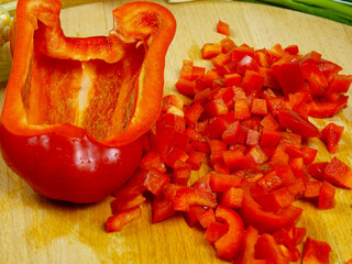Chopped raw red bell peppers into small pieces, half of pepper are on wooden cutting board, a making of a salad