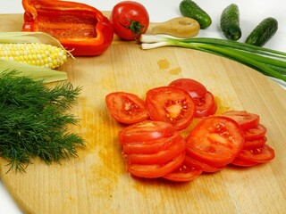 Sliced  raw red tomato, various vegetables are on wooden cutting board, a making of a salad