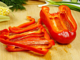 Sliced  raw red bell peppers,  half of pepper are on wooden cutting board, a making of a salad
