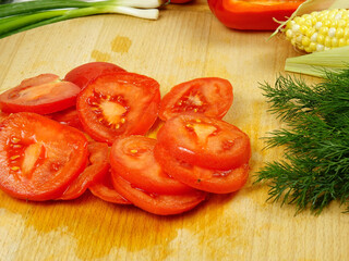 Sliced  raw red tomato, various vegetables are on wooden cutting board, a making of a salad